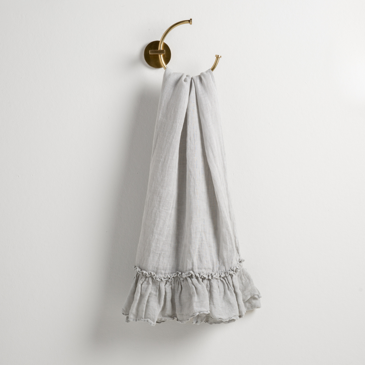 Cloud: guest towel draped through a decorative brass towel ring, against a white wall.