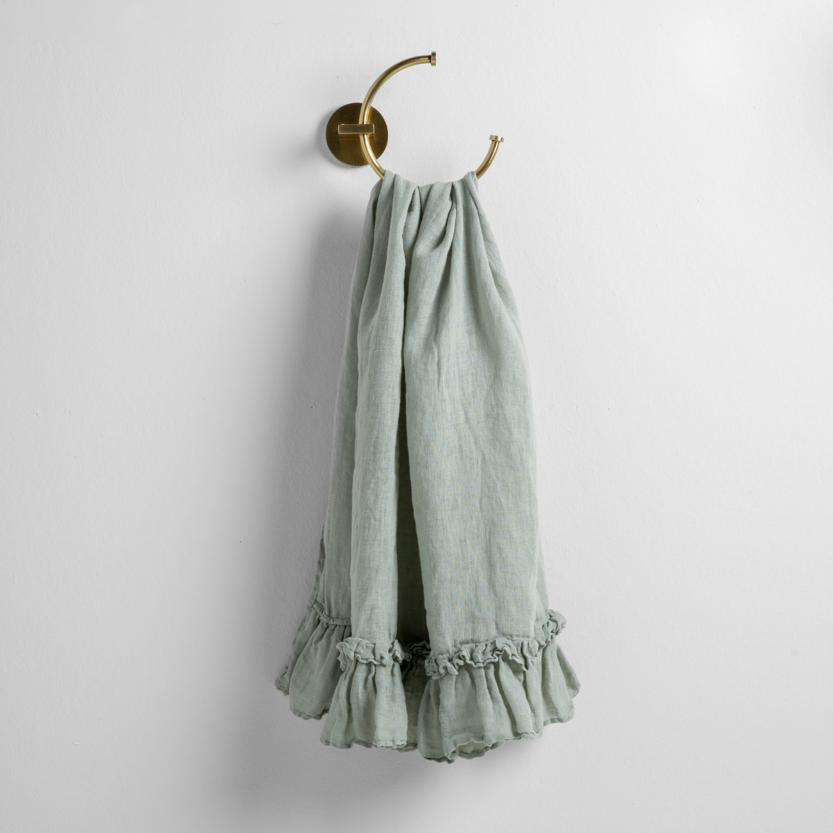 Eucalyptus: guest towel draped through a decorative brass towel ring, against a white wall.
