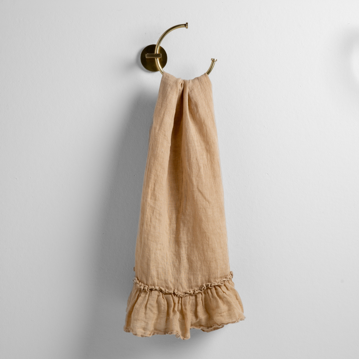 Honeycomb: guest towel draped through a decorative brass towel ring, against a white wall.