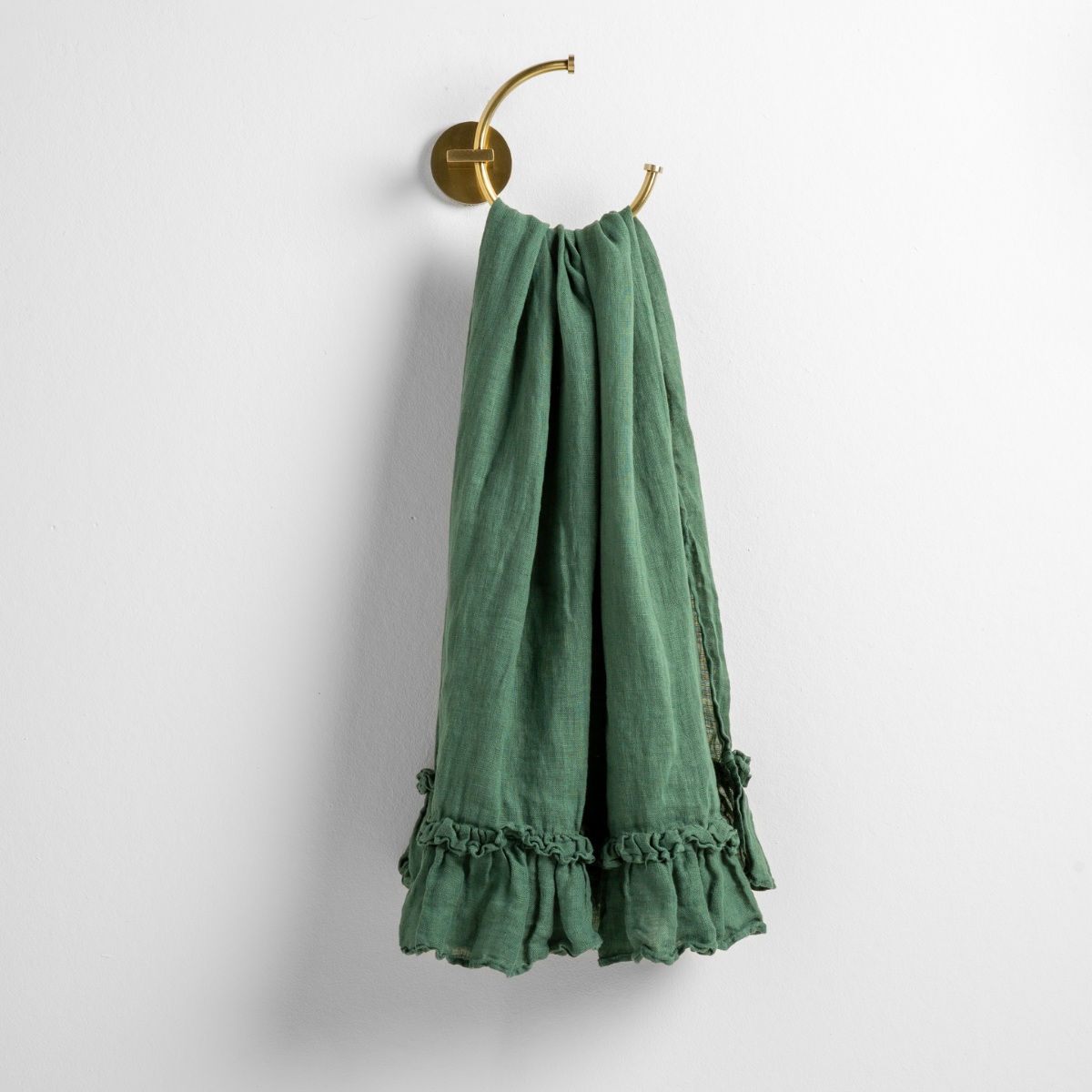 Jade: guest towel draped through a decorative brass towel ring, against a white wall.
