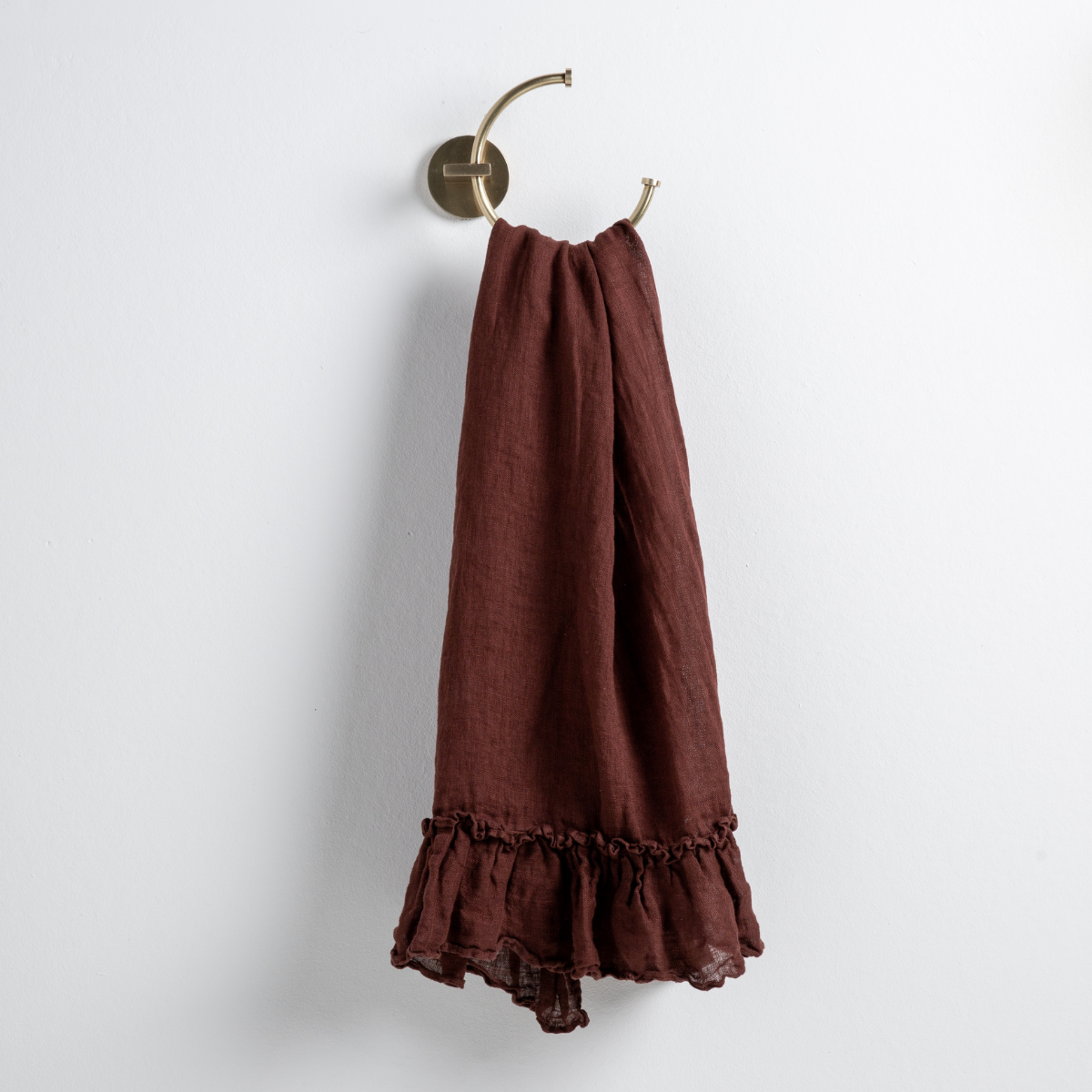 Mahogany: guest towel draped through a decorative brass towel ring, against a white wall.