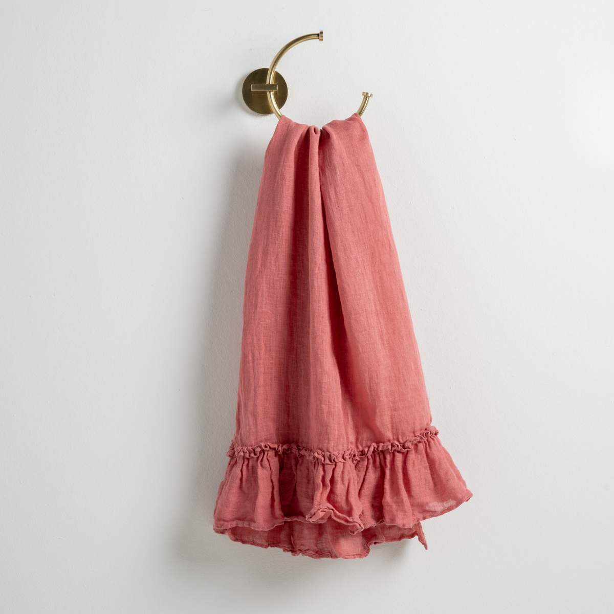 Poppy: guest towel draped through a decorative brass towel ring, against a white wall.