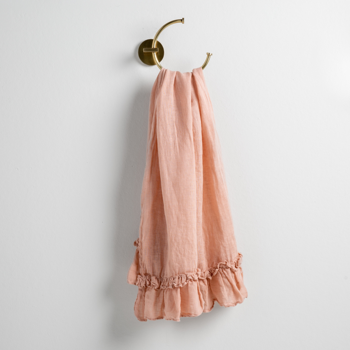 Rouge: guest towel draped through a decorative brass towel ring, against a white wall.