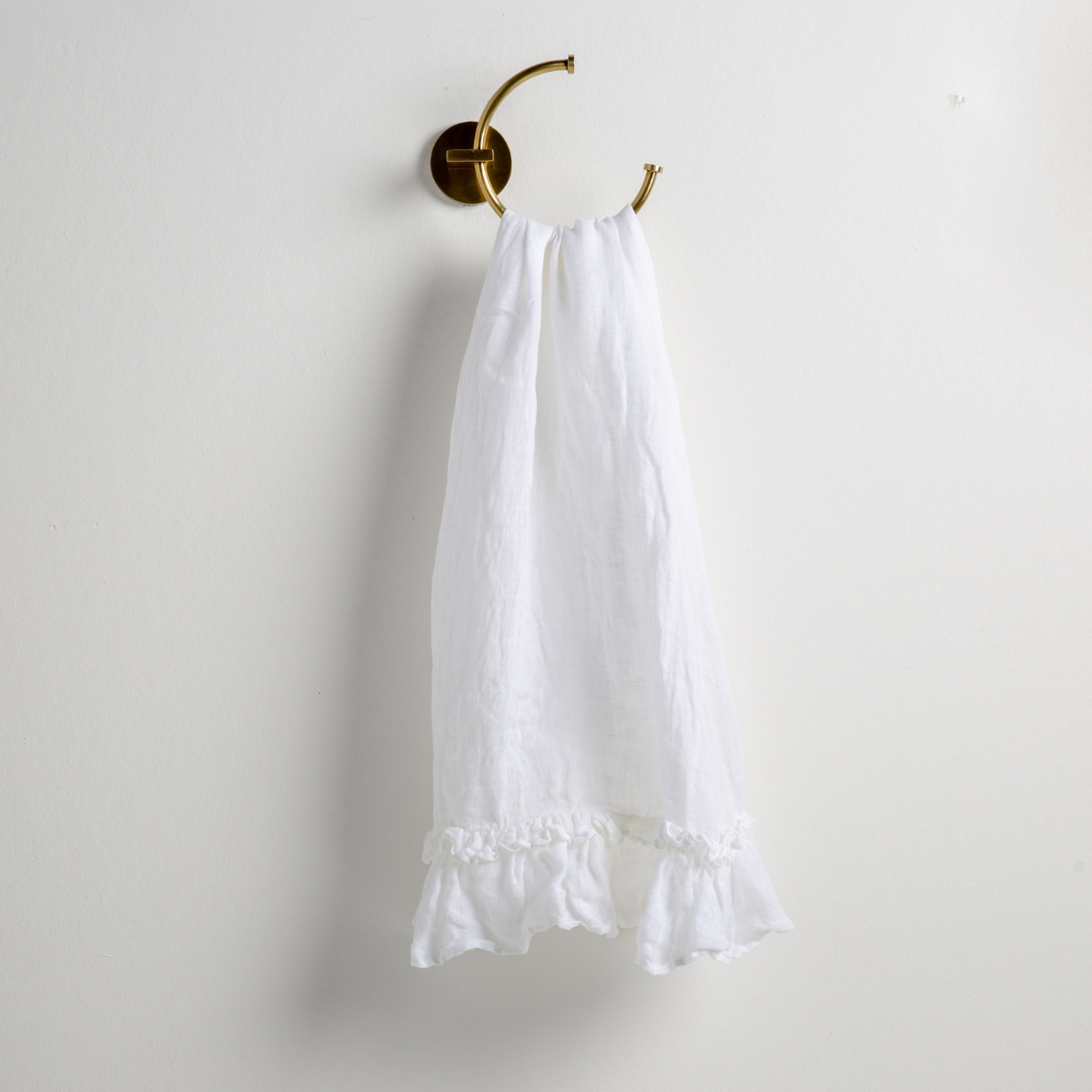 White: guest towel draped through a decorative brass towel ring, against a white wall.