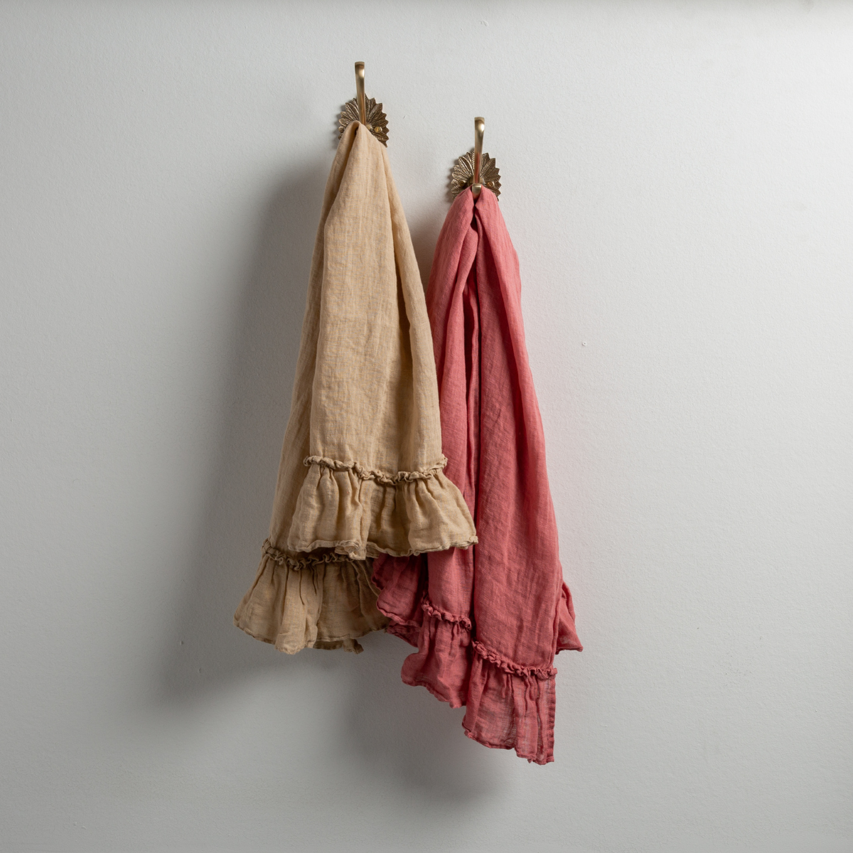 : Two Linen Whisper guest towels, draped over decorative hooks against a white wall - honeycomb and poppy.