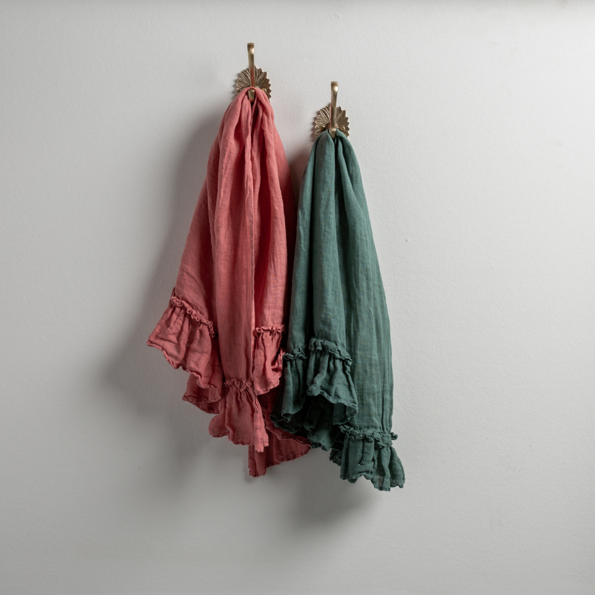 : Two Linen Whisper guest towels, draped over decorative hooks against a white wall - poppy and jade.