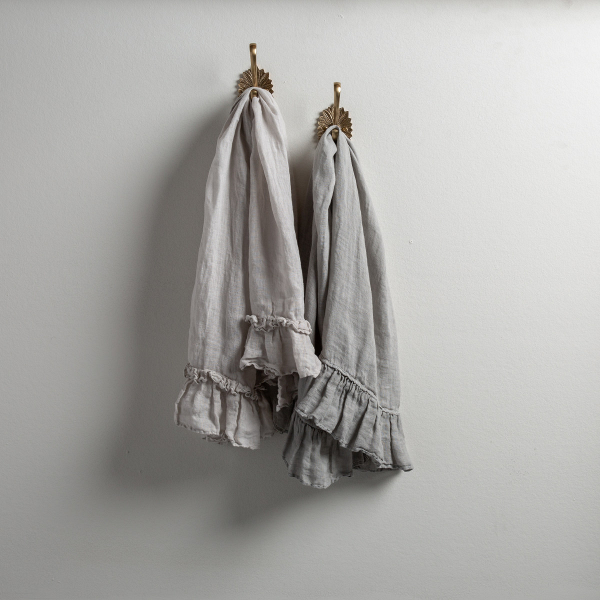 : Two Linen Whisper guest towels, draped over decorative hooks against a white wall - sterling and mineral.