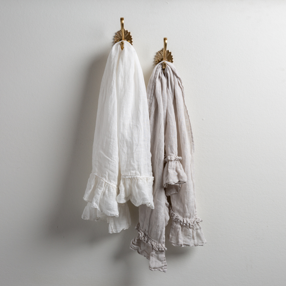 : Two Linen Whisper guest towels, draped over decorative hooks against a white wall - white and sterling.