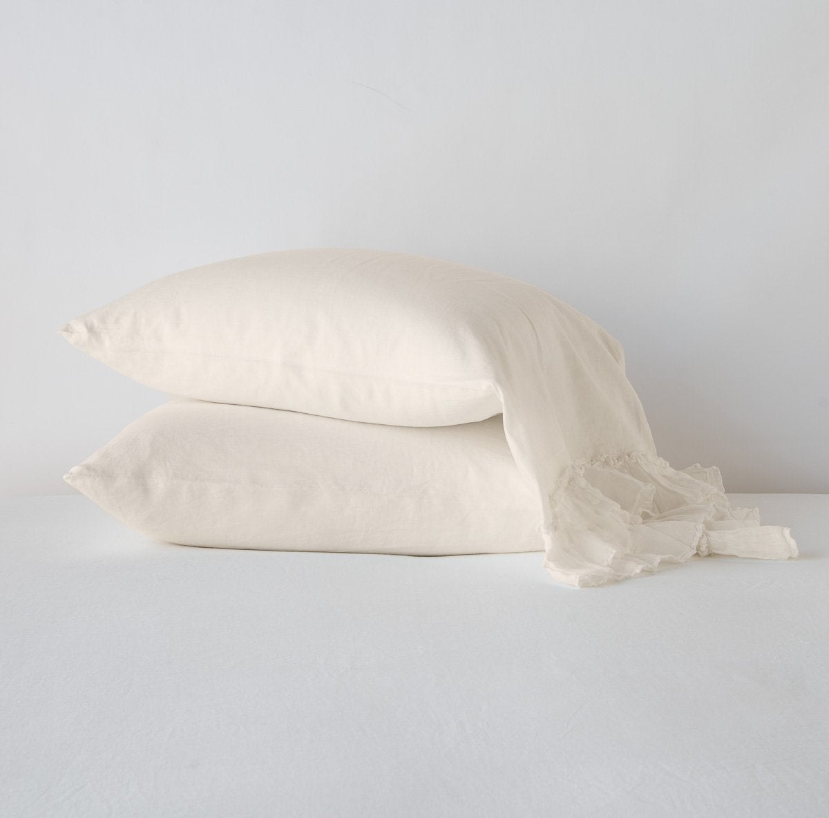 Parchment: Two sleeping pillows stacked at a slight angle against a plain background, showcasing ruffle trim detail - side view.