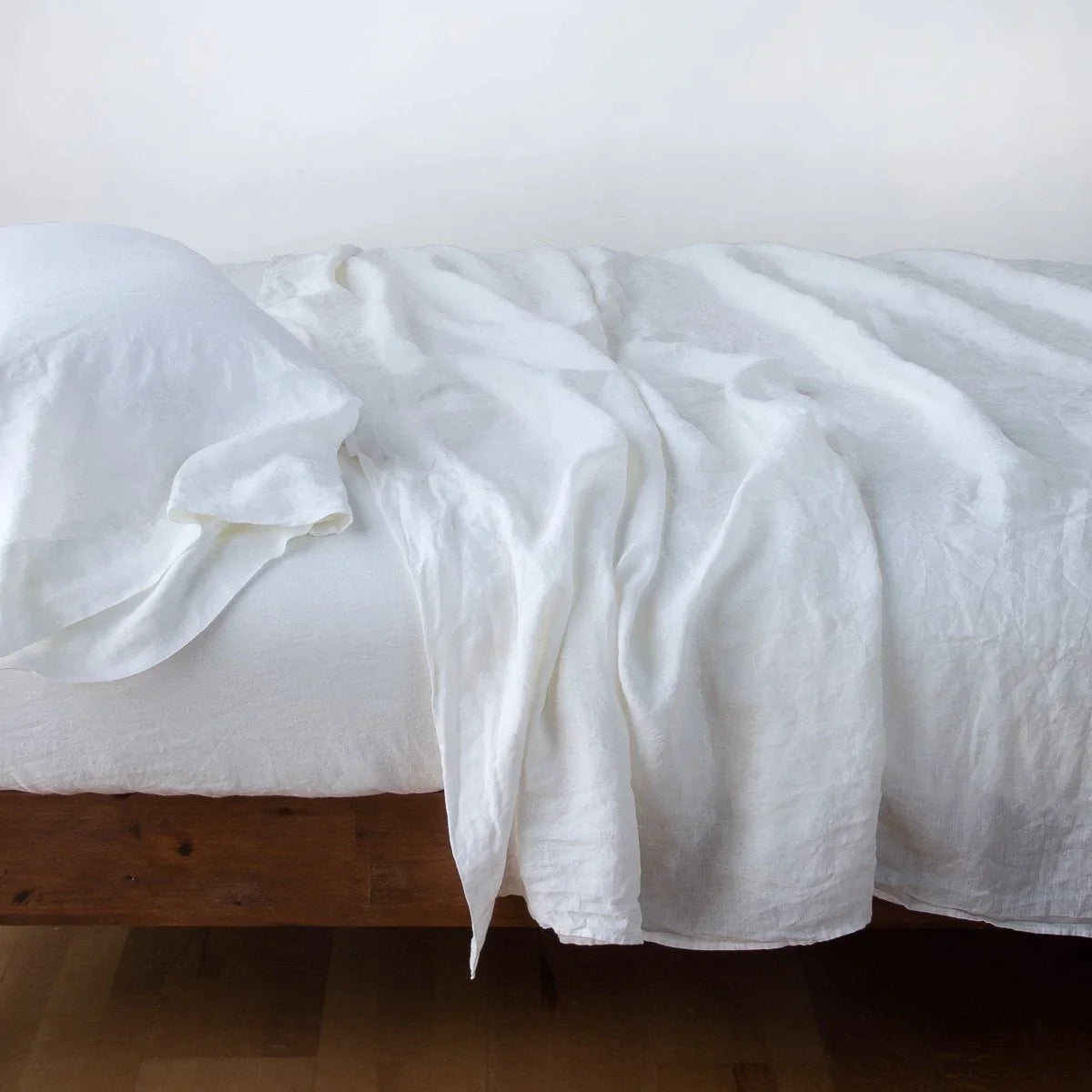 White: fitted sheet with matching rumpled flat sheet and sleeping pillow - side view.