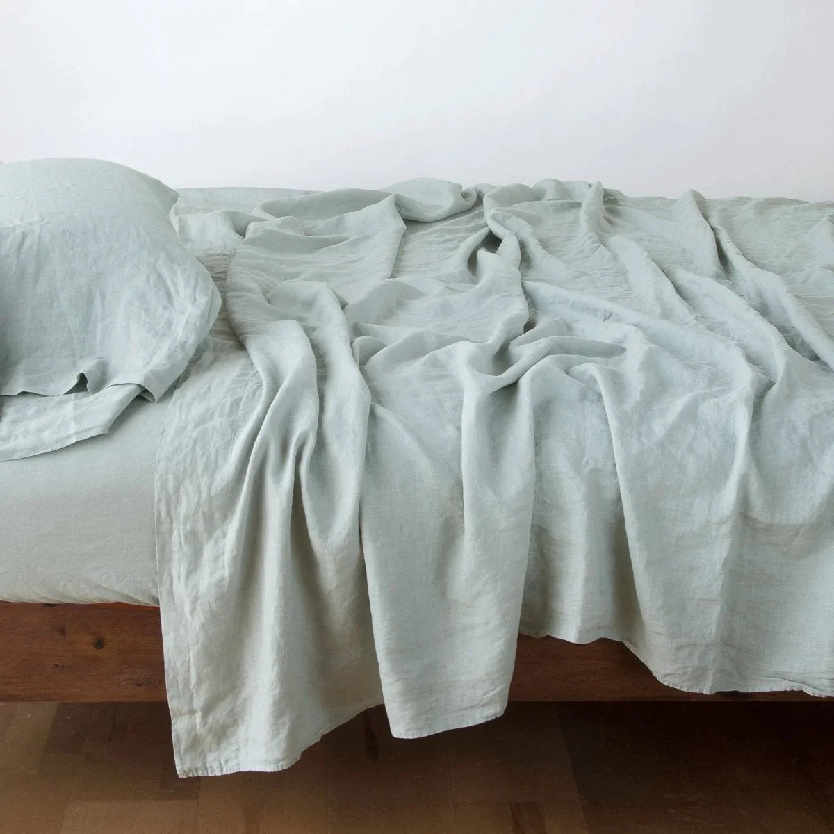 : Rumpled linen flat sheet in eucalyptus, with matching fitted sheet and sleeping pillow - side view.