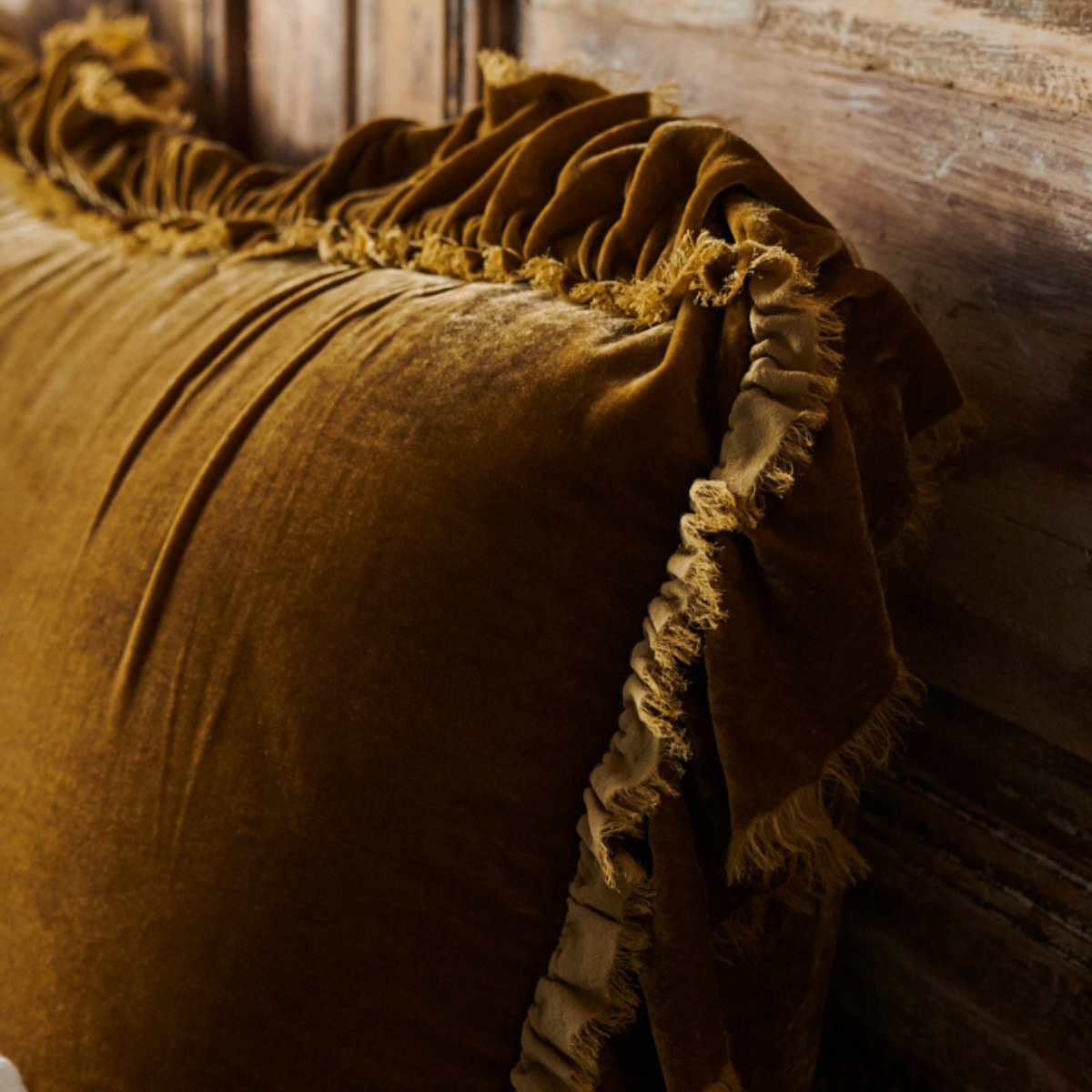 : Close-up of Loulah sham ruffle detail - showcasing the 4 inch silkvelvet ruffle with raw-edge eyelash detail - shone in honeycomb against a distressed wood headboard.