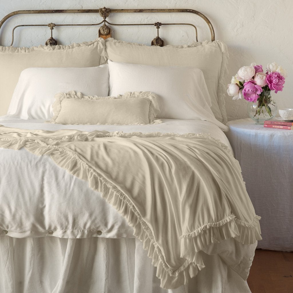 Parchment: throw blanket draped over the end of a white bed, shown with matching accent pillow - end of bed view.