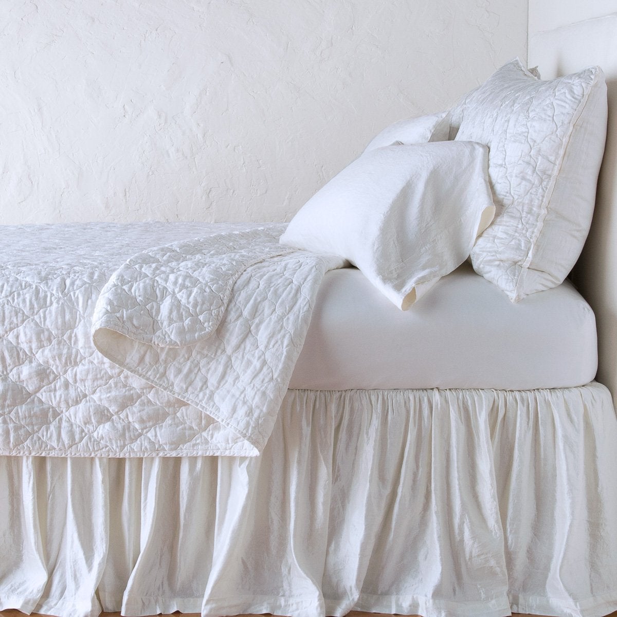 White: coverlet neatly folded back to reveal linen reverse, on a monochromatic bed - side view.