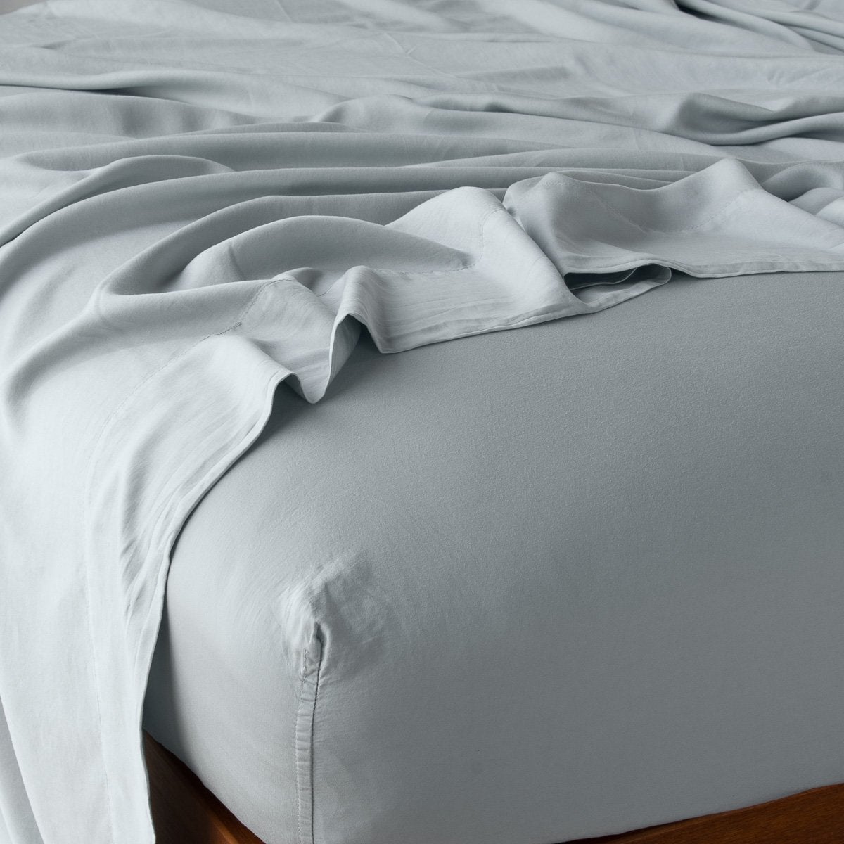 : Rumpled flat sheet layered over a matching fitted sheet - mineral, angled view from top corner.