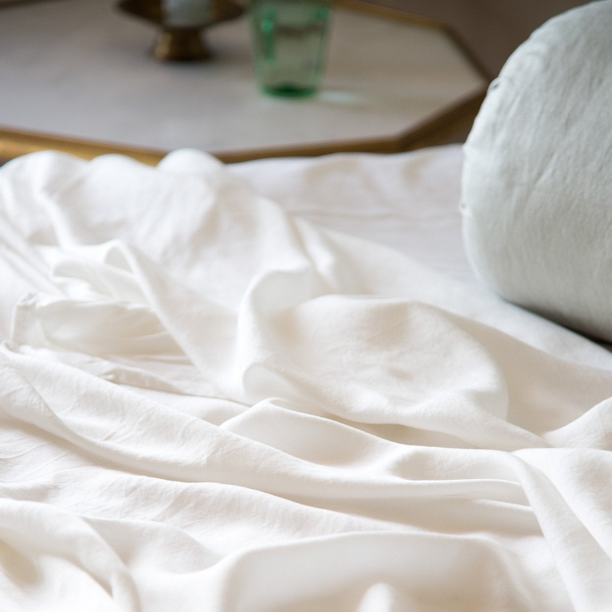 [allvariants]: Close-up of Madera Luxe flat sheet in winter white, softly luminous against a shimmery light blue silk charmeuse bolster.