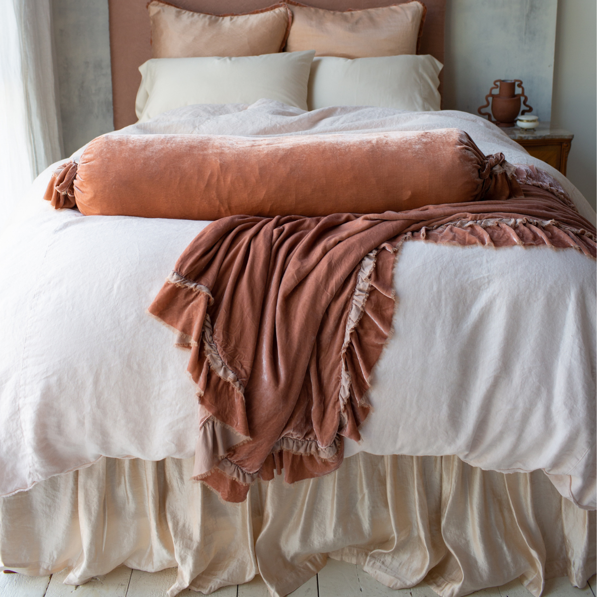 [allvariants]: Paloma bed skirt and matching shams add subtle shine to linen and cotton bedding accented with ruffled silk velvet, all in pink and cream tones - end of bed view.