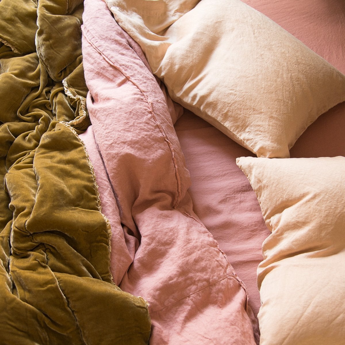 : Soft pink Paloma sleeping pillows and linen bedding with rich gold silk velvet, lightly rumpled - overhead view.