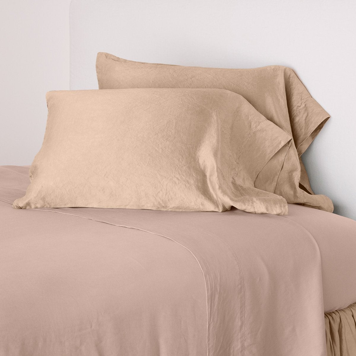 Rouge: sleeping pillows leaning upright against a white wall on monochromatic sheeting - cropped three-quarter angle.