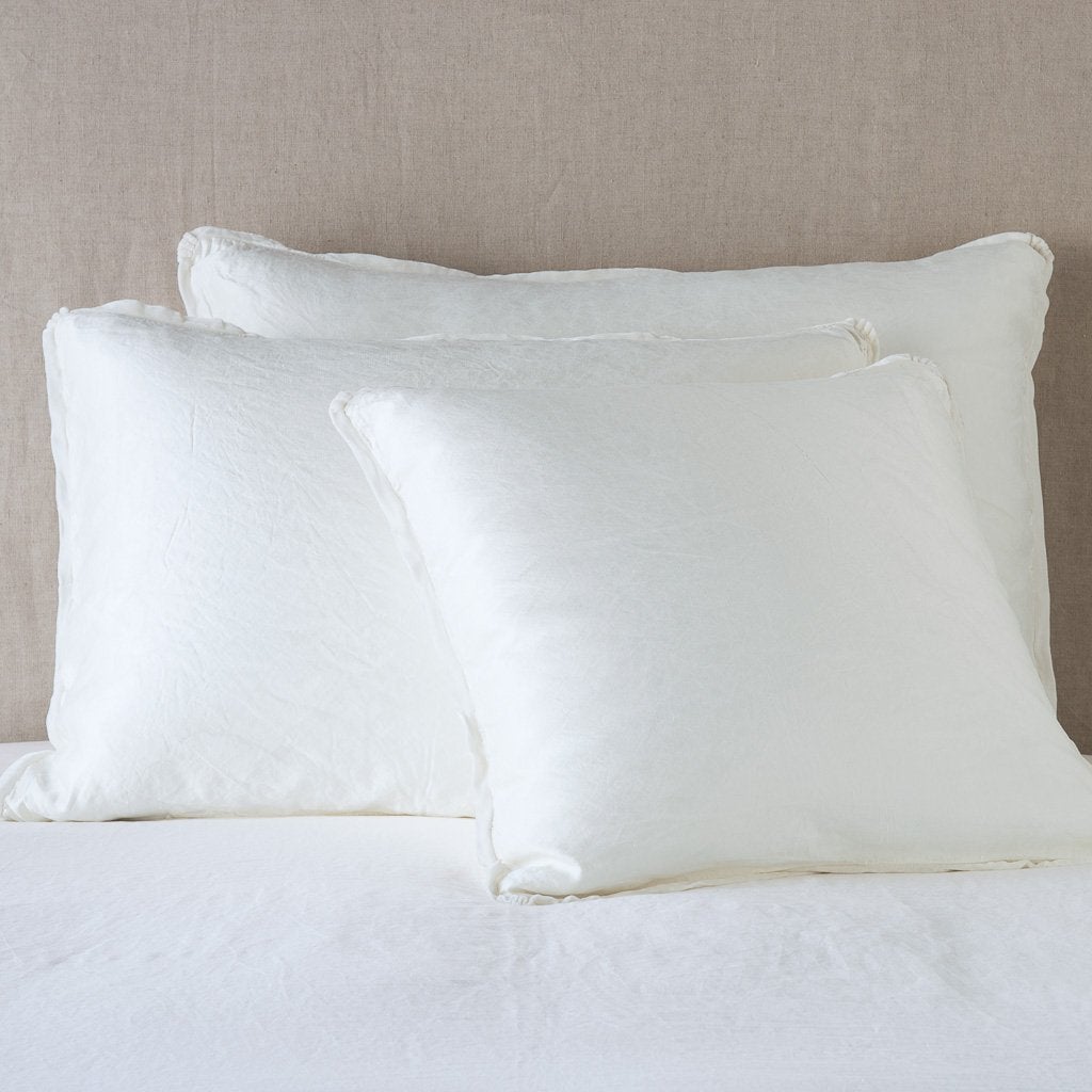Winter White: shams leaning upright on white sheeting against a neutral headboard.