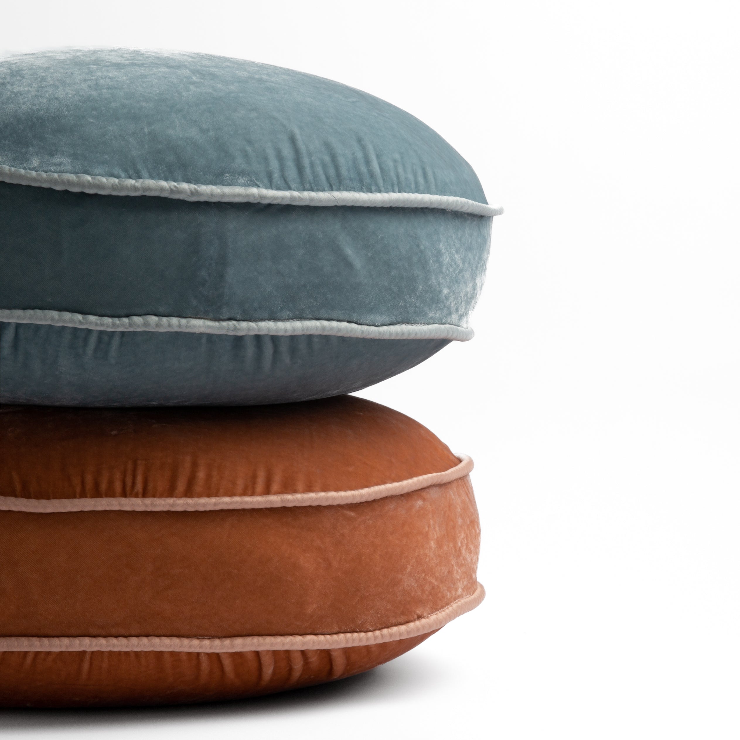 : two silk velvet round pillows stacked in cloud and rouge against a white background. 