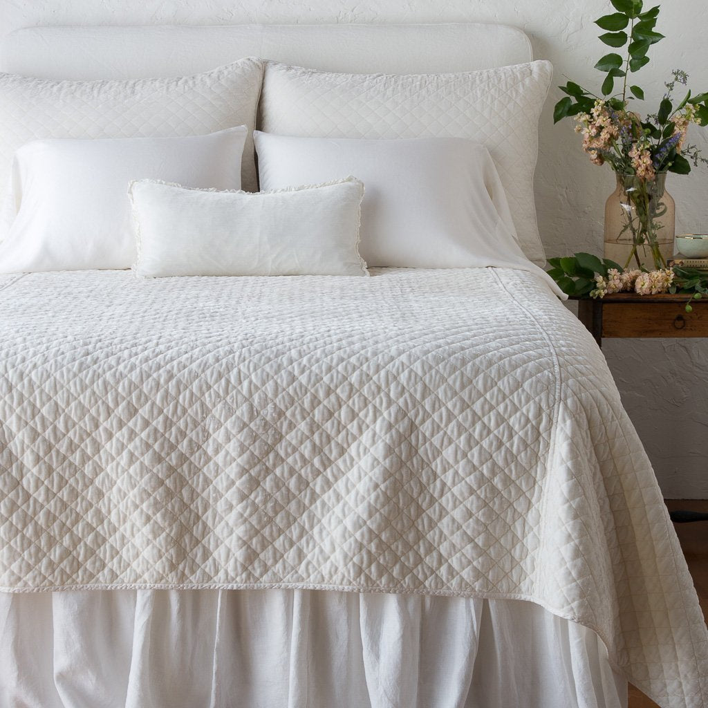 [allvariants]: Silk velvet quilted coverlet on a neatly made, winter white bed - end of bed view.