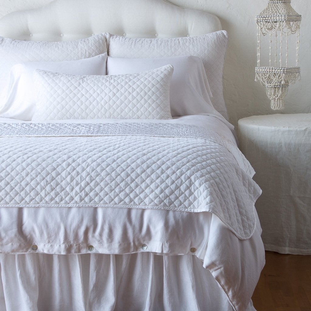 White: 16x36 pillow and matching throw blanket on a white, neatly made bed - end of bed view.