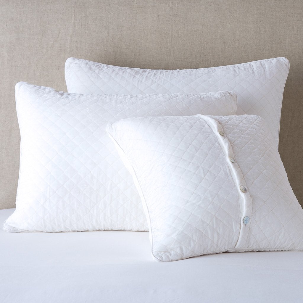 White: shams leaning upright against a neutral headboard. One sham is backwards to showcase the shimmering shell button closure.
