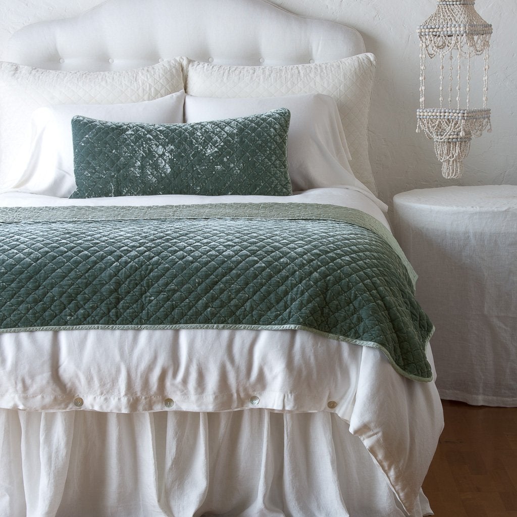 Eucalyptus: throw blanket and matching lumbar pillow on a neatly made white bed - end of bed view.
