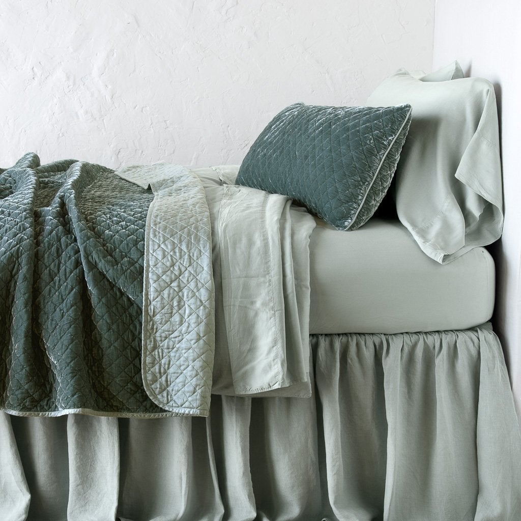 Eucalyptus: throw blanket rumpled and folded back, featuring satin back. Shown with matching lumbar pillow and monochromatic sheeting - side view.
