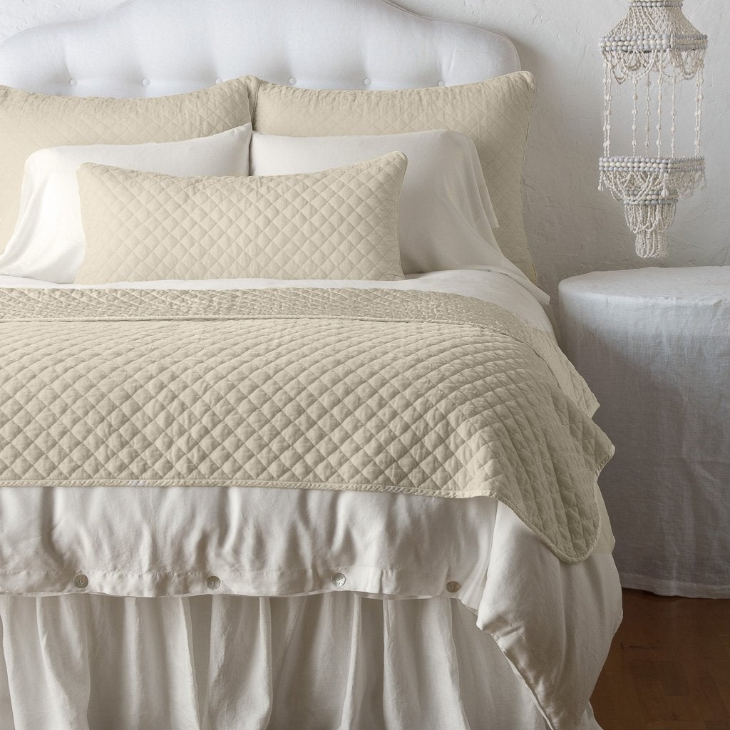 Parchment: throw blanket and matching lumbar pillow on a neatly made white bed - end of bed view.