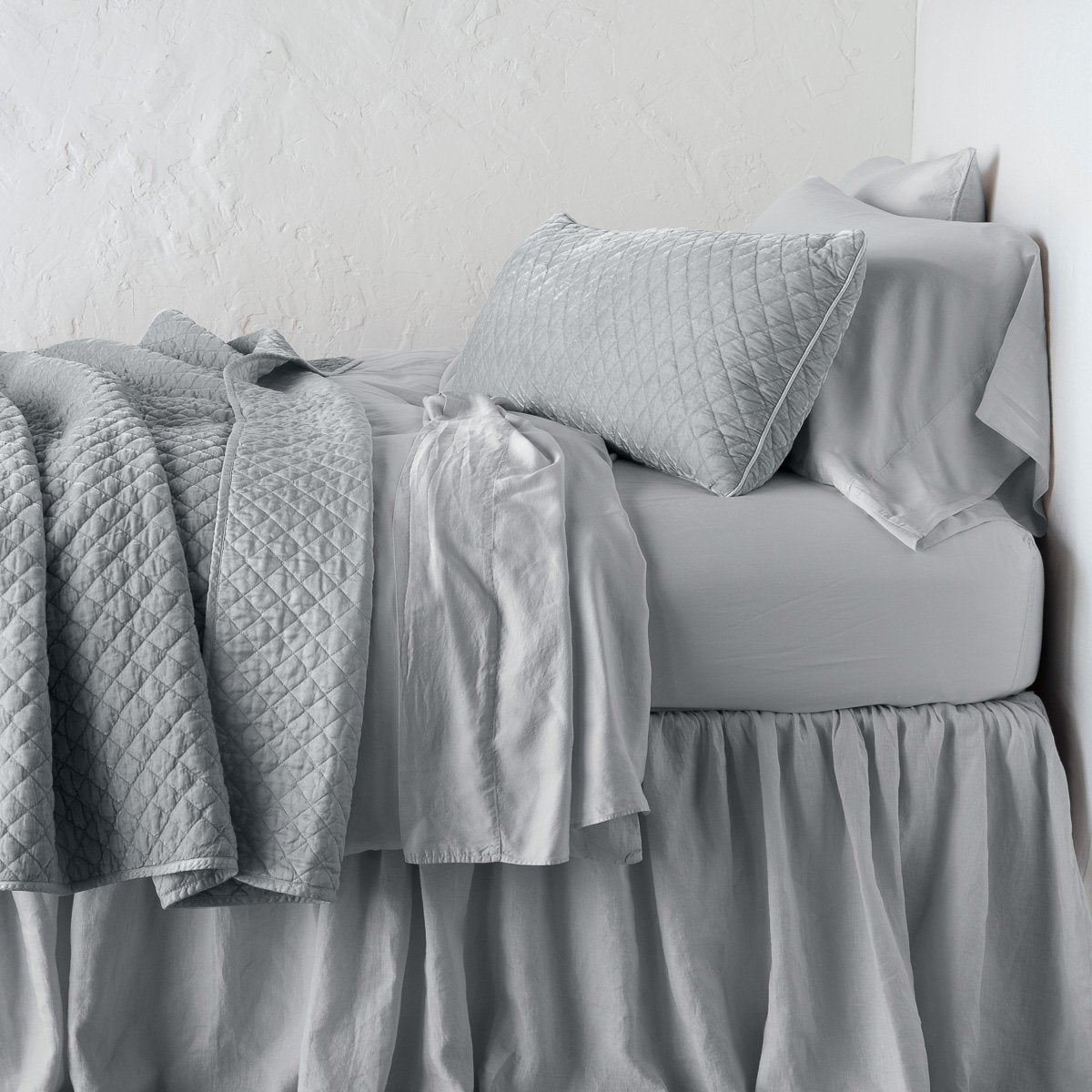 Sterling: throw blanket rumpled and folded back, featuring satin back. Shown with matching lumbar pillow and monochromatic sheeting - side view.