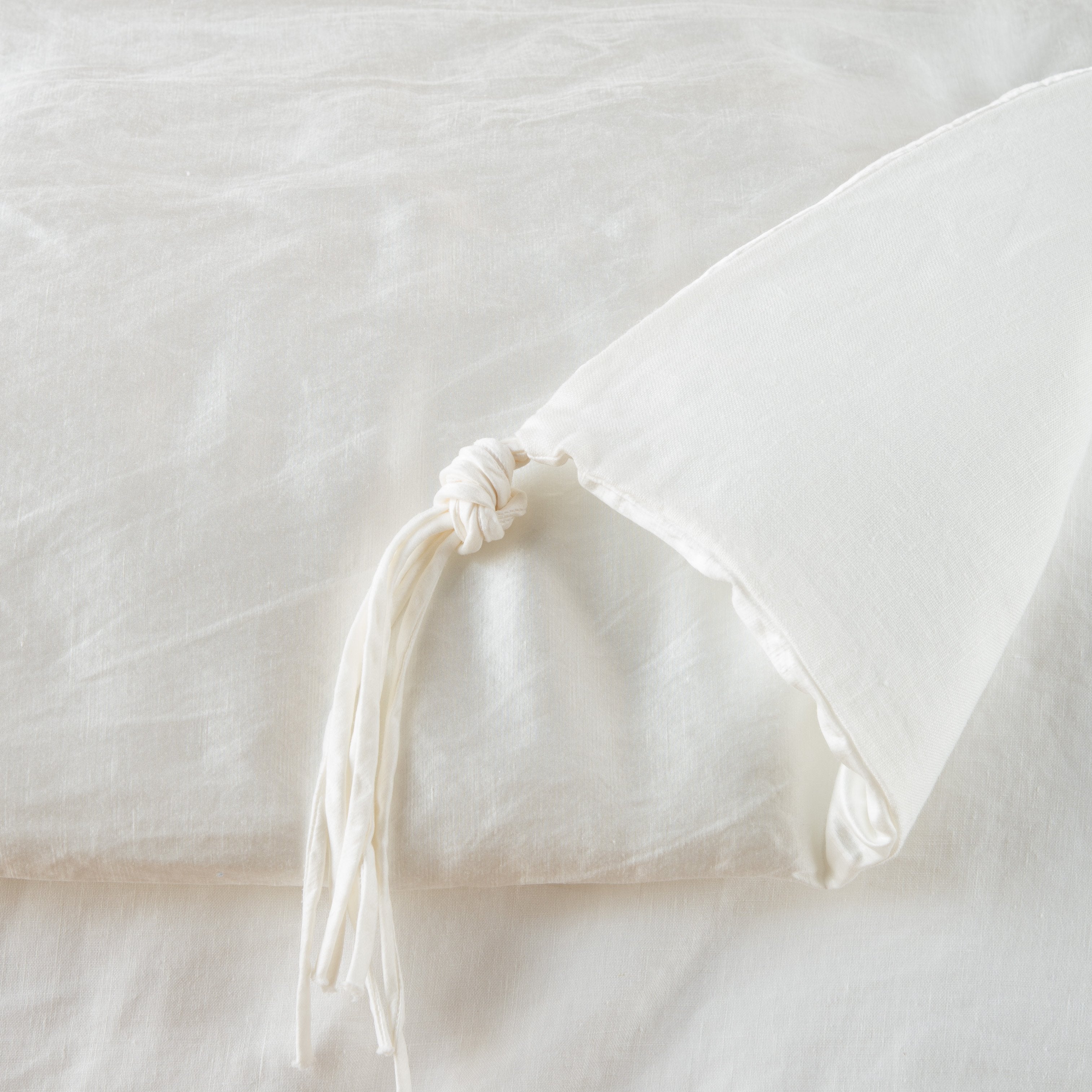 Winter White: Close up of blanket, with a corner turned back to showcase the midweight linen back and corner tassel - overhead view.