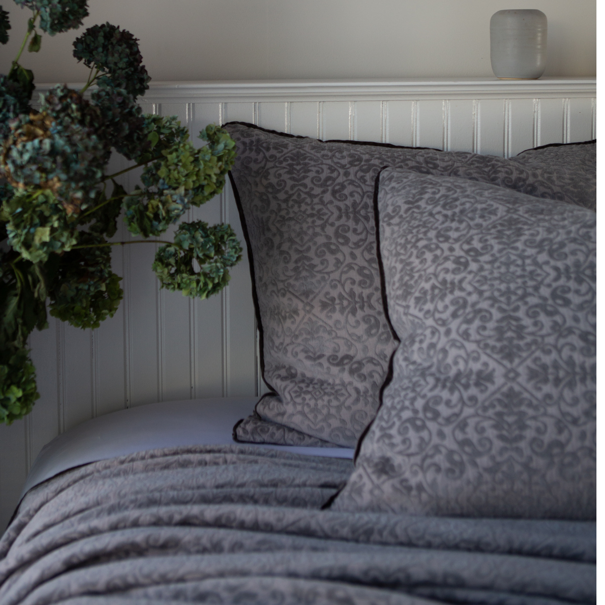 : Vienna shams and coverlet in moonlight against a white beadboard wall. Cropped head-on angle showcases silk velvet trim detail.