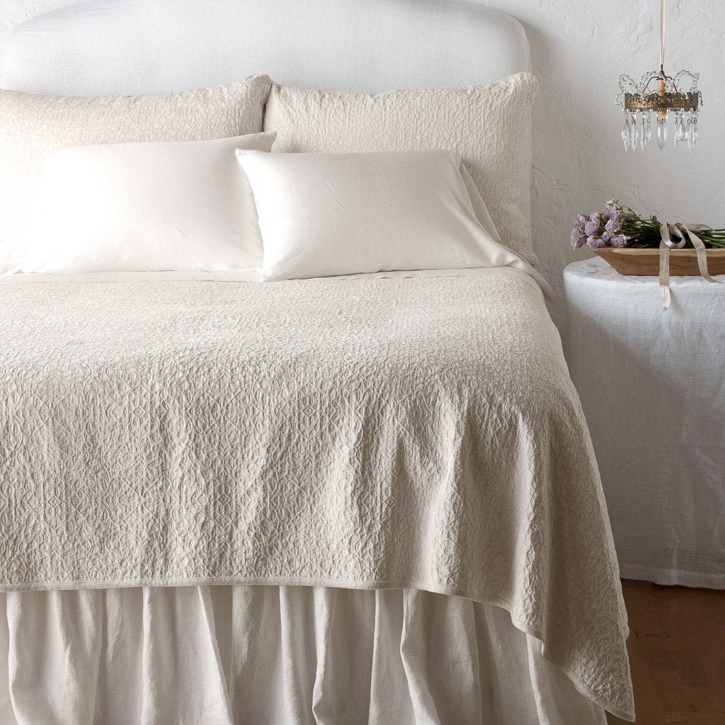 : Vienna coverlet and shams on a monochromatic, neatly made bed - parchment, end of bed view.