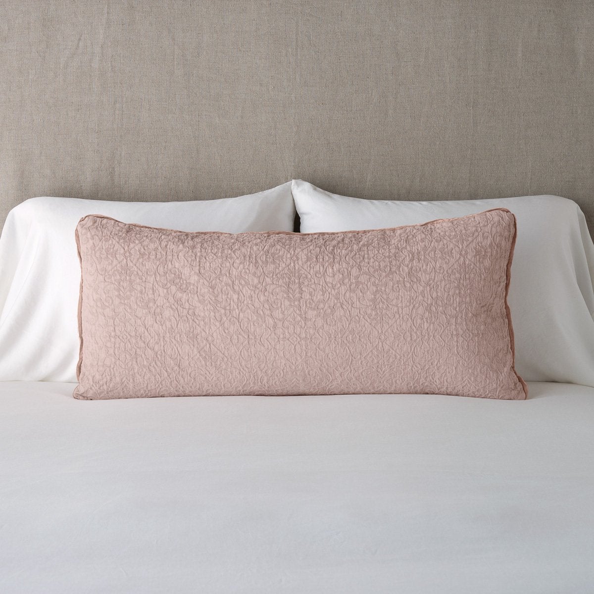 Rouge: 16x36 pillow leaning upright against white sleeping pillows on a neutral headboard.