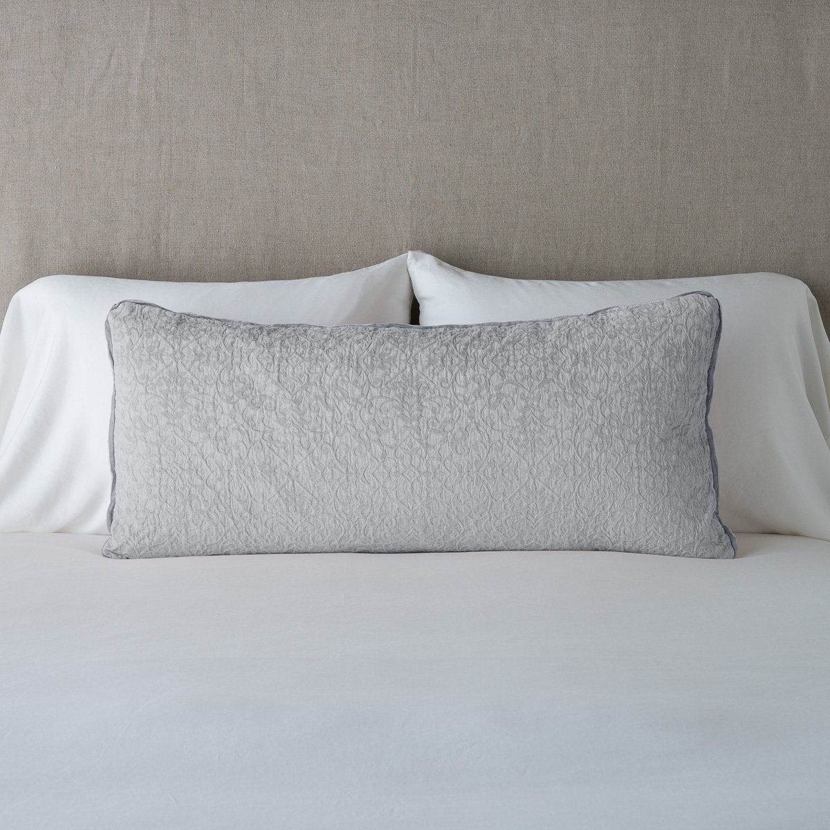 Sterling: 16x36 pillow leaning upright against white sleeping pillows on a neutral headboard.